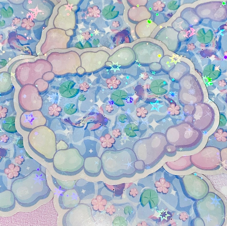 Puede incluir: Un conjunto de pegatinas iridiscentes con un dise&ntilde;o caprichoso de peces koi nadando en un estanque rodeado de rocas y nen&uacute;fares de colores pastel. Las pegatinas tienen un acabado hologr&aacute;fico que brilla a la luz.
