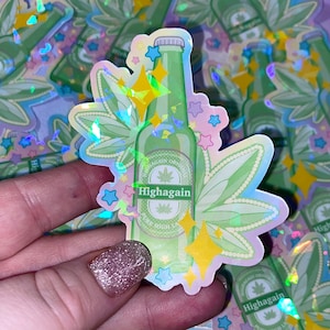 May include: A holographic sticker featuring a green beer bottle with the text "Highagain" and a marijuana leaf. The bottle is surrounded by green leaves and stars.