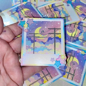 May include: A holographic sticker featuring a night sky with a crescent moon, stars, and power lines. The sticker has a glittery, iridescent finish and is framed with a white border.