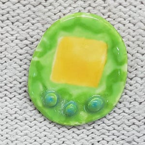 May include: A green ceramic pendant with a yellow square in the centre and three blue circles around the bottom.