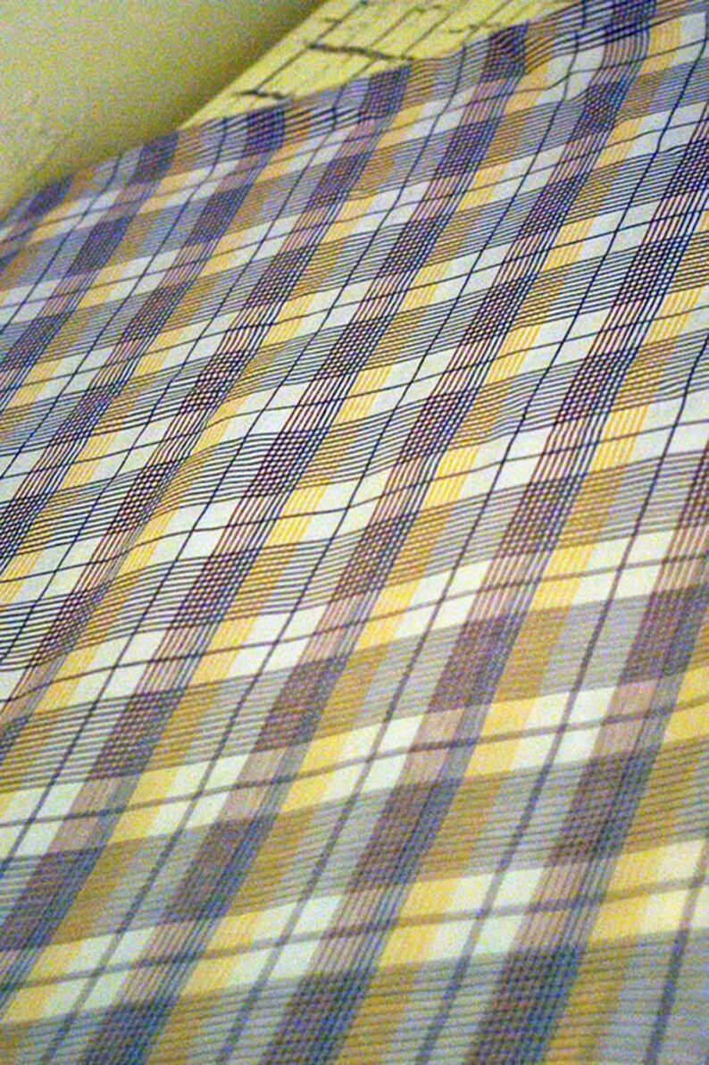 May include: A white fabric with a checkered pattern in shades of yellow, blue, and brown.