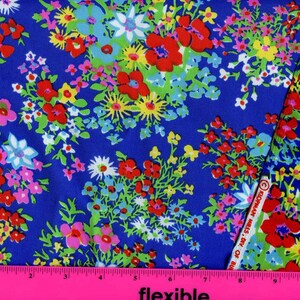 K&ouml;nnte beinhalten: Blauer Stoff mit einem Blumendruck mit roten, rosa, wei&szlig;en, gelben und gr&uuml;nen Blumen. Der Stoff wird mit einem rosa Lineal gemessen.