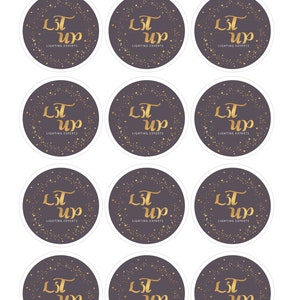 May include: A collection of round stickers with a dark gray background and gold text. The text reads "Lit Up" in a stylized font, with "Lighting Experts" below. Gold stars and dots surround the text.