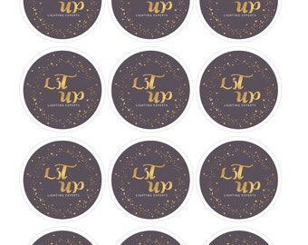May include: A collection of round stickers with a dark gray background and gold text. The text reads "Lit Up" in a stylized font, with "Lighting Experts" below. Gold stars and dots surround the text.