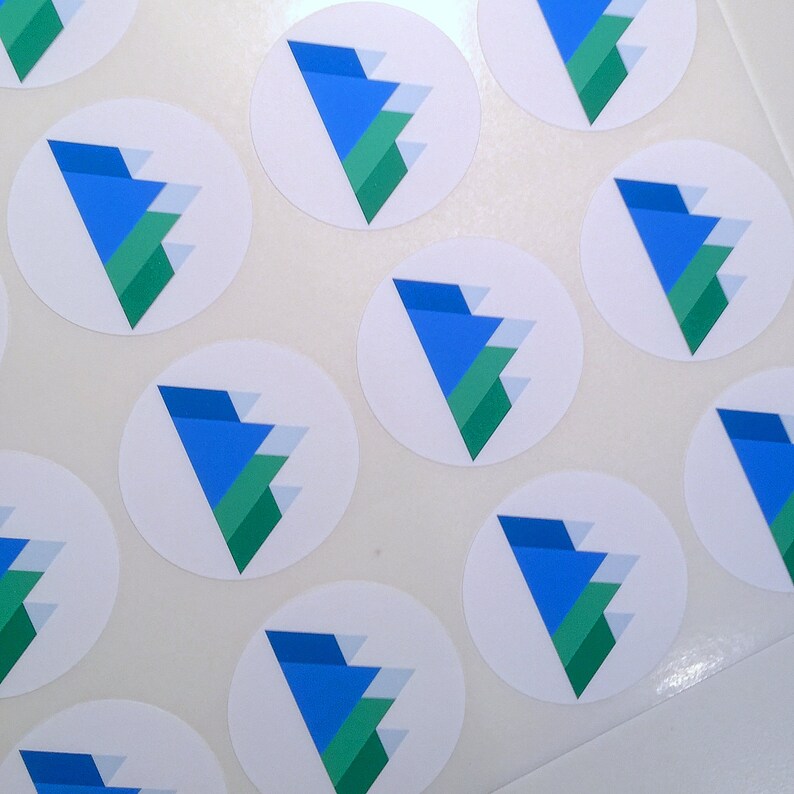 May include: A collection of white, circular stickers. Each sticker features a blue, green, and white geometric design. The design is a stylized, layered triangle. The stickers are arranged on a white surface.
