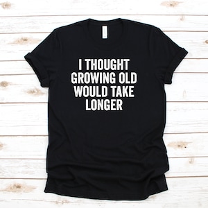 Puede incluir: Camiseta negra con texto blanco que dice "Pensé que envejecer llevaría más tiempo".