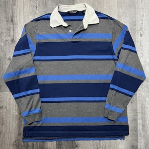 May include: A long-sleeve rugby shirt featuring horizontal stripes in shades of grey, navy blue, and light blue. The shirt has a solid white collar, a buttoned placket with a single visible white button, and the Rountree & Yorke brand label.