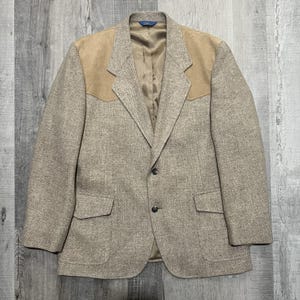 May include: A tan tweed blazer with suede shoulder patches. The jacket has two front pockets and a two-button closure. The interior lining is a light tan color. The blazer is a classic style.