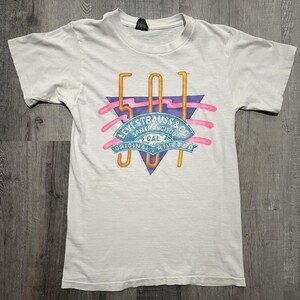 May include: White t-shirt with a colorful graphic design. The design features the number "501" in orange, a blue triangle, and the text "LEVI STRAUSS & CO. SAN FRANCISCO CAL. ORIGINAL RIVETED" in a banner.