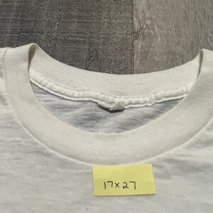 Puede incluir: Camiseta blanca de cuello redondo con una etiqueta que dice "17 x 27".