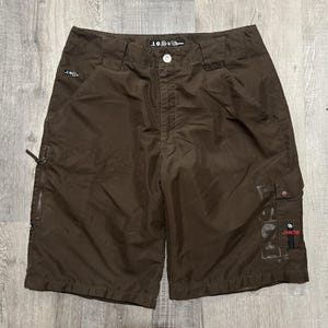 May include: Brown cargo shorts with multiple pockets and a zip closure. The shorts feature the text "108" on the waistband and "FORCE" printed on the leg. The shorts have a button closure and a relaxed fit.