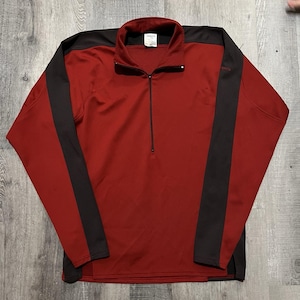 May include: A red long-sleeve pullover with a black collar and black stripes down the sleeves. The pullover has a quarter-zip closure and a small logo on the chest. The material appears to be a lightweight, athletic fabric.
