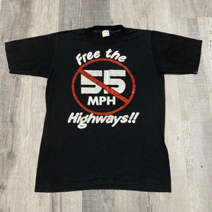 May include: Black t-shirt with a white graphic of a red circle with a diagonal line through it. The circle has the text "55 MPH" inside. The text "Free the Highways!!" is below the circle.