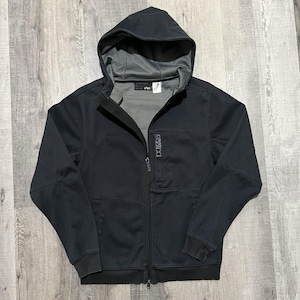 May include: Black zip-up hooded jacket with a gray interior lining. The jacket features a hood, a full-length zipper, and the word "Dakine" printed on the chest. The jacket is made of a durable material.