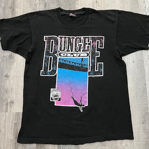 May include: Black t-shirt with a graphic of a person bungee jumping off a bridge. The graphic includes the text "Bungee Club" and "Bungee Jumping Adventure".