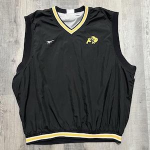 May include: Black sleeveless vest with a V-neck and a yellow and white striped hem. The vest has a yellow and white trim around the neckline and armholes. A yellow and black logo is on the chest, and a Reebok logo is on the left side.