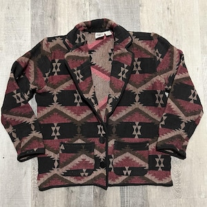 May include: A patterned blazer in shades of black, burgundy, and brown. The jacket features a geometric design, a notched collar, two front pockets, and two black buttons. The blazer is a medium weight and appears to be made of a woven fabric.