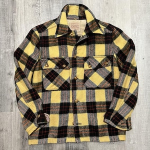 May include: A yellow, black, and red plaid jacket with two chest pockets and button closures. The jacket has a collared neckline and long sleeves. The fabric appears to be a thick wool or wool blend.