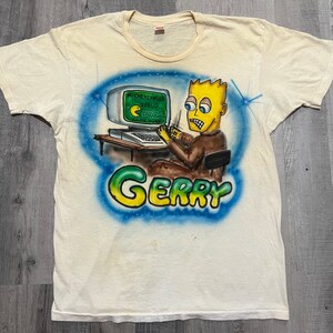 May include: A white t-shirt with a blue, green, and yellow airbrushed design of a cartoon character sitting at a computer. The computer screen says "Michelangelo Virus" and "Game Over". The text "Gerry" is written below the character.