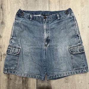 May include: Light blue denim cargo shorts with two side pockets and a button and zipper closure. The shorts have a classic, casual style and are made of a durable denim fabric.