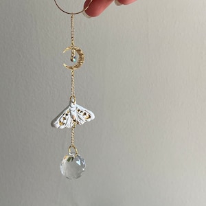 May include: A gold chain with a crescent moon charm, a white porcelain moth charm, and a clear crystal prism hanging from a gold hoop.