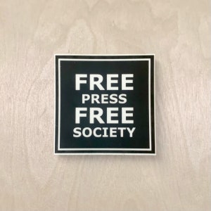May include: A black and white sticker with the text "FREE PRESS FREE SOCIETY" on a white background.