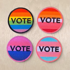 May include: Four round embroidered patches with the word "VOTE" in black lettering on a multi-coloured background. The patches are in the colours of the rainbow, transgender, lesbian, and bisexual pride flags.