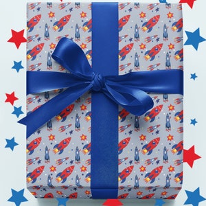 May include: A blue gift box with a red and blue rocket ship pattern. The box is tied with a blue ribbon and surrounded by red and blue stars.
