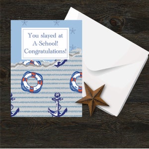 May include: A blue and white card with a torn edge. The card has a nautical theme with anchors and life preservers. The text on the card reads "You slayed at A-School! Congratulations!"