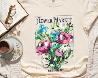 Puede incluir: Una camiseta beige con un estampado gráfico de un ramo de flores coloridas. El gráfico incluye el texto "FLOWER MARKET" y "KING SMITH ART".