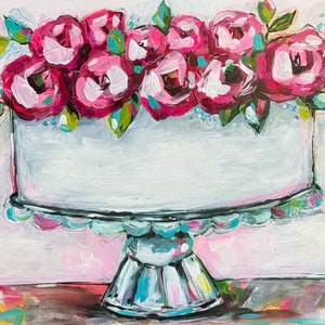 以下が含まれることがあります： ピンクと白の花が飾られた白いケーキが、青と白のケーキスタンドの上に置かれています。ケーキはピンクと白の背景の上にあります。