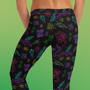 Könnte beinhalten: Schwarze Leggings mit einem bunten Muster aus Insekten, Schmetterlingen und Skorpionen. Das Muster ist in Neonfarben umrandet.
