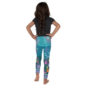 K&ouml;nnte beinhalten: Ein junges Kind tr&auml;gt eine tealfarbene Leggings mit einem Blumen- und Schmetterlingsmuster. Die Leggings hat ein dunkles und helles Teal-Farbschema mit rosa, gelben und violetten Akzenten.