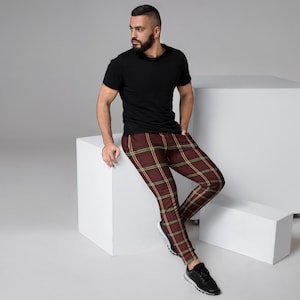 May include: Maroon plaid joggers with a yellow and white grid pattern. The pants are cuffed at the ankles. The person in the image is wearing a black t-shirt and black sneakers.