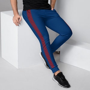 Puede incluir: Pantalones deportivos azules con una raya roja en el lateral. Los pantalones deportivos son de color azul liso con una raya roja en el lateral de cada pierna. La persona lleva zapatillas negras.