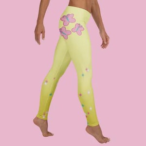 Op de afbeelding: Gele legging met een gradiënteffect, versierd met roze en paarse vlindergraphics aan de bovenkant en sterrenpatronen. De legging is nauwsluitend en gemaakt van een glad materiaal.