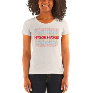 May include: A white t-shirt with a repeating pattern of the word "hygge" in red, blue, and yellow. The word "hygge" is in red in the center of the pattern.
