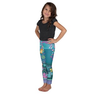 K&ouml;nnte beinhalten: Ein M&auml;dchen tr&auml;gt ein schwarzes T-Shirt mit kurzen &Auml;rmeln und eine tealfarbene Leggings mit einem bunten floralen und geometrischen Muster.