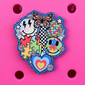 May include: A colorful charm featuring a butterfly, smiley faces, puzzle pieces, a disco ball, and a heart. The charm has a blue glitter border and is set against a bright pink background.