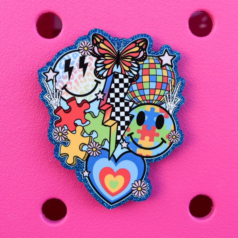 May include: A colorful charm featuring a butterfly, smiley faces, puzzle pieces, a disco ball, and a heart. The charm has a blue glitter border and is set against a bright pink background.