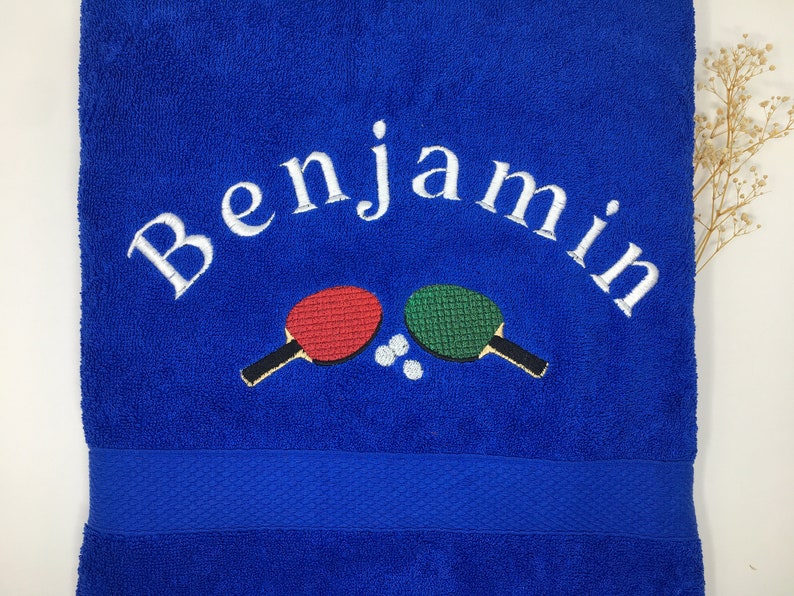 May include: Blue towel with white embroidery that says "Benjamin" and two embroidered ping pong paddles with a white ball in between.