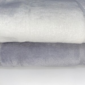May include: Two towels, one white and one gray, are folded on top of each other. The towels are soft and fluffy.
