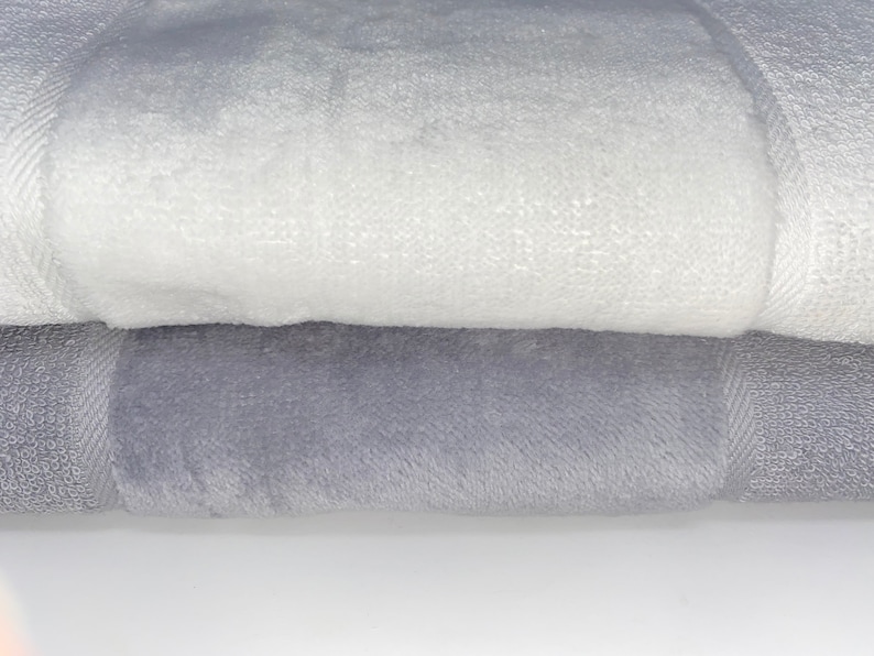 May include: Two towels, one white and one gray, are folded on top of each other. The towels are soft and fluffy.
