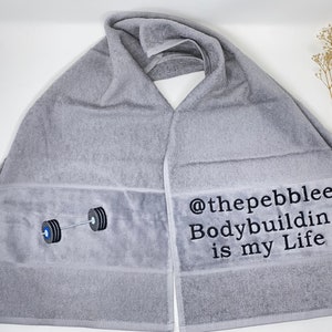May include: Gray cotton towel with black embroidery. The embroidery includes a barbell with weights and the text "@thepebblee Bodybuilding is my Life".