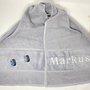 May include: Gray bath towel with a white barbell design and the name "Markus" embroidered on it.