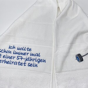 May include: White towel with blue embroidery that reads "Ich wollte schon immer mal mit einer 57-j&auml;hrigen verheiratet sein" and a gray barbell.