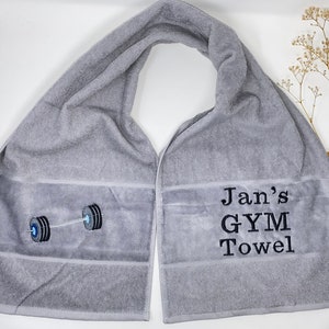May include: Gray gym towel with the text "Jan's GYM Towel" and a black and white embroidered image of a barbell.
