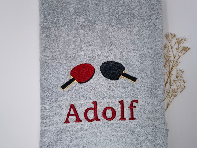 May include: Gray towel with red and black embroidered ping pong paddles and the name "Adolf" in red embroidery.