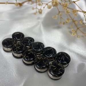 May include: A set of eight black and gold magnetic clasps. The clasps are round and have a marbled pattern. They are ideal for holding together fabric or other materials.