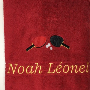 May include: Red towel with embroidered ping pong paddles and the name "Noah L&eacute;onel" in gold thread.